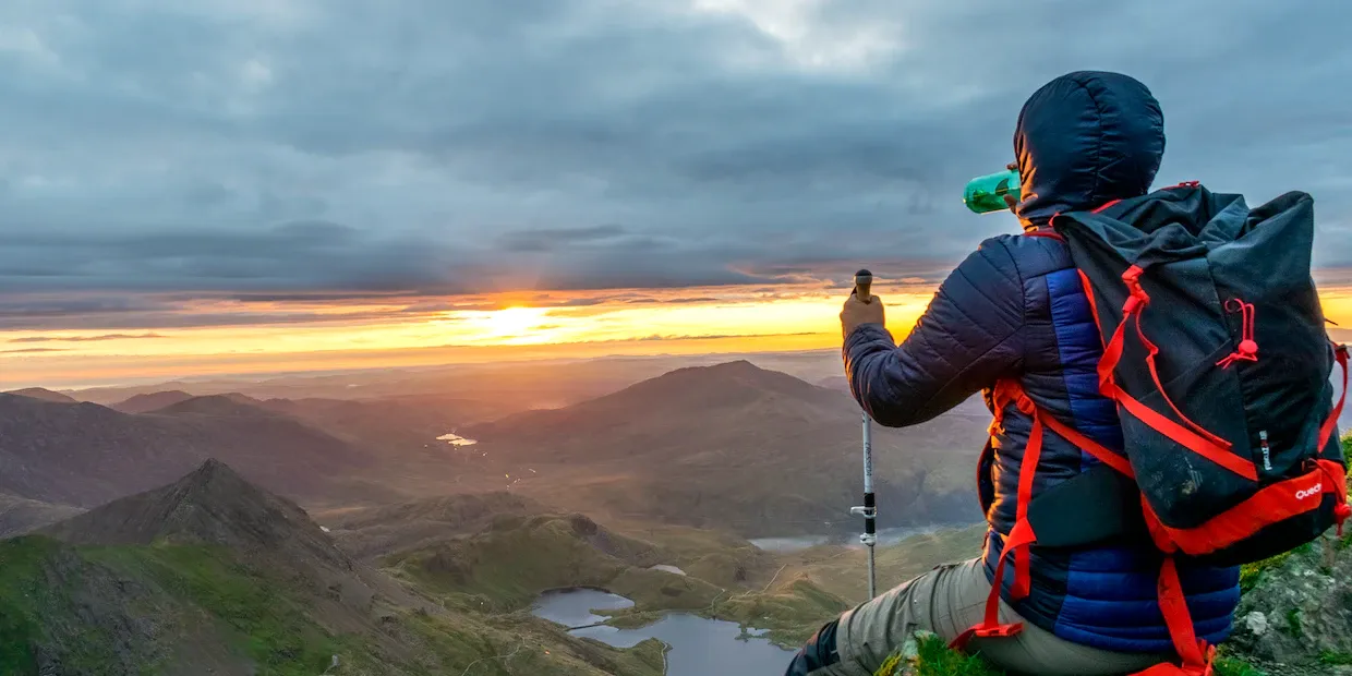 A pair of trekking poles planted on a rocky mountain trail at sunrise